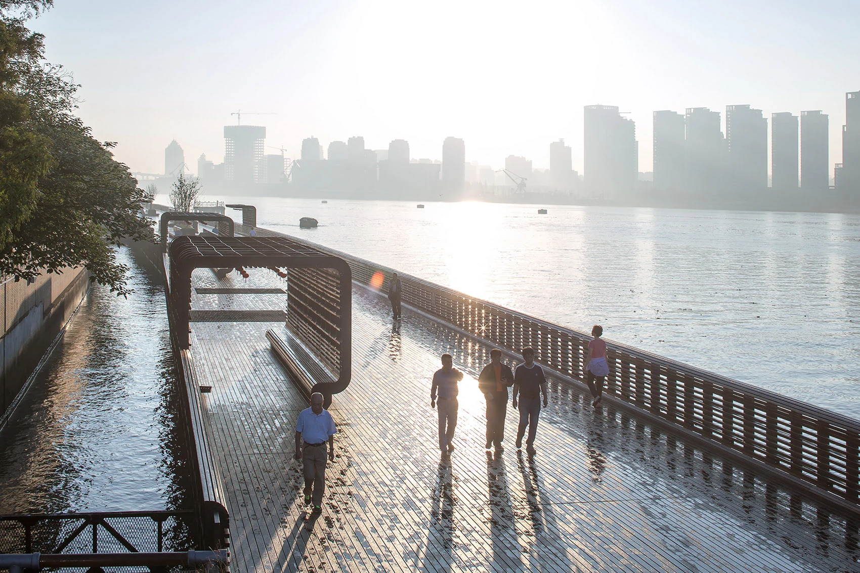 Visitors walking beside water and restored industrial structures at sunset